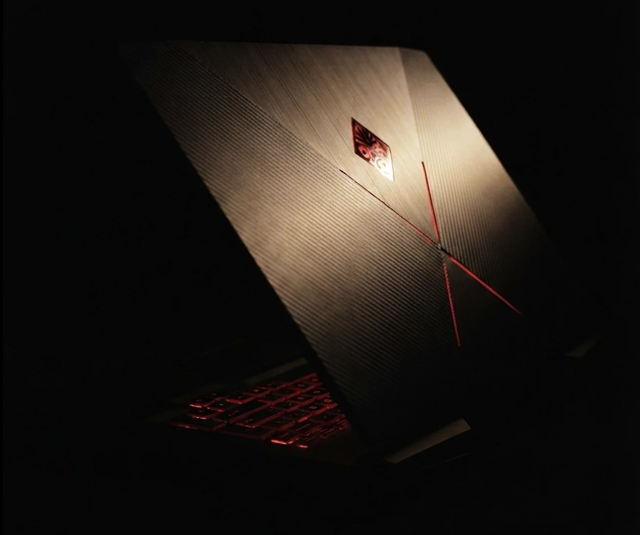 Bucephalus — the HP OMEN laptop half-open in darkness, the edge of the lid catching the light, the Omen logo and keyboard backlit in red.
